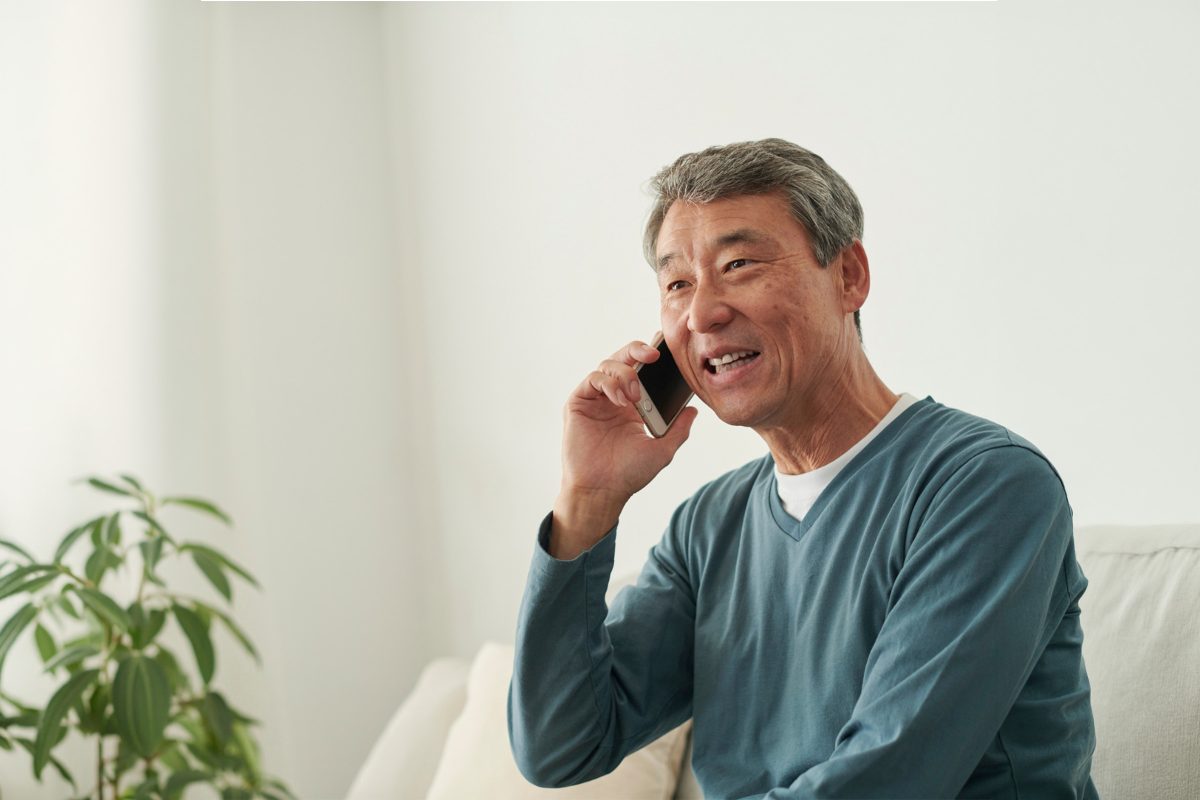 En person sitter ner och har sin mobiltelefon mot örat. Pratar och ser glad ut.